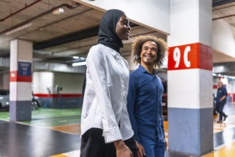 Diverse young couple walking happily and smiling together in a modern underground parking garage