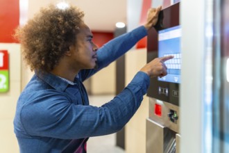 Young man standing, pointing finger at a digital touchscreen on an automated vending machine,