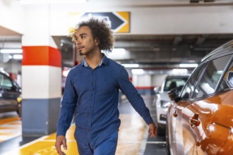 Young man with afro hair walks through a brightly lit underground parking garage, glancing right as