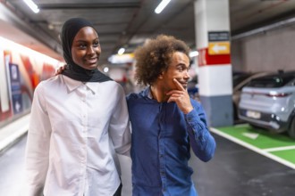 Diverse young couple happily walking arm in arm through a modern underground parking garage,