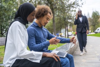 Young diverse colleagues collaborating on a portable computer in an urban park, with a woman in the