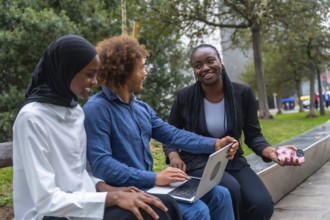 Diverse group of young adult students smiling and collaborating on a laptop in a city park,