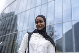 African american woman student wearing a black hijab and white shirt, carrying a backpack, standing
