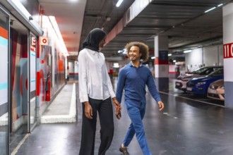 Diverse young couple walking hand in hand through an underground parking garage, sharing a loving