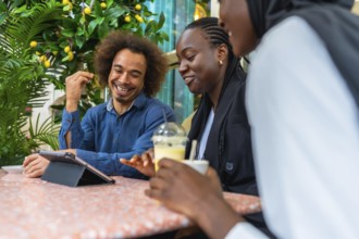 Cheerful diverse friends sitting at a cafe table, laughing and discussing content on a digital