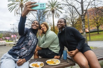 Diverse group of young adult friends smiling while taking a cheerful selfie and eating take out