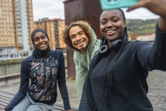 Three smiling diverse young adults enjoying friendship and making a selfie outdoors in an urban