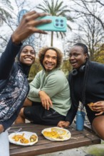 Diverse group of young adult friends smiling and laughing, holding a phone to take a selfie while