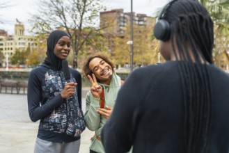 Young black woman wearing a hijab interviewing a smiling friend making a peace sign, while another