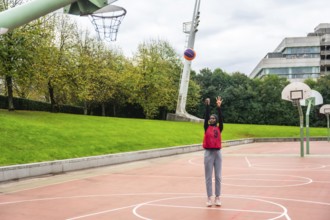 Muslim woman wearing a hijab and sportswear on an urban basketball court shooting a colorful ball,
