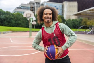 Young man with afro hairstyle smiling and holding a colorful basketball while standing on an