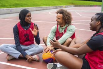 Group of young adult friends from different backgrounds sitting on a basketball court, taking a