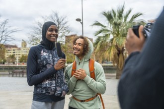 Female journalist interviewing a young, happy man with diverse background, holding a microphone