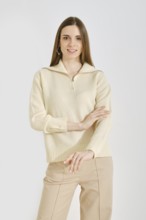 Cheerful woman in a light cream sweater and beige pants posing over white background. The outfit