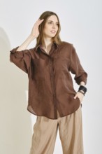A woman showcases a stylish outfit with a brown button-up shirt and light beige pants, perfect for