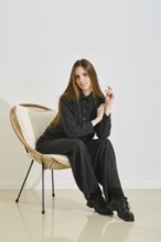 A young woman sits stylishly in a cozy chair, dressed in a trendy, practical outfit that highlights