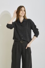 A young woman playfully touch her smooth long hair wearing trendy outfit featuring a dark button-up