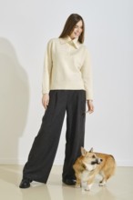 Playful woman in ivory sweater and loose pants playing with her corgi dog in bright room