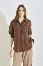 A woman in a stylish brown shirt paired with light pants, highlighting a trendy outfit suitable for