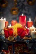 Two glasses of mulled wine with cinnamon and oranges in front of red and white candles, Christmas