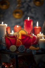 Hot mulled wine with cinnamon sticks and oranges on a Christmassy background with candles