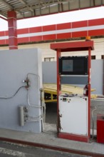 Red gas pump with screen and cables in front of a grey wall, gas filling station, Sewan,