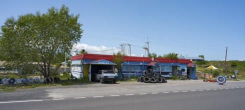 Auto repair shop next to the road with stacked tires and vehicles surrounded by quiet countryside,