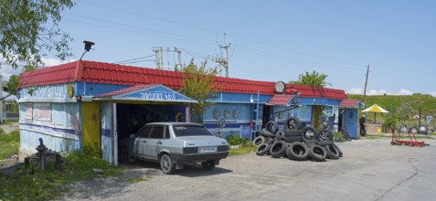 Auto repair shop with stacked tires and vehicles surrounded by rural surroundings under blue skies,