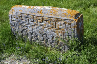 Ancient tombstone set in grass with complex carvings and orange patina, Noratus cemetery, Noradus,