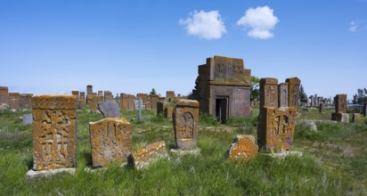 Ancient cemetery with decorated tombstones and a small building under a blue sky, crossstones,
