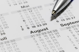 Close-up of a calendar with ballpoint pen pointing to the month of August