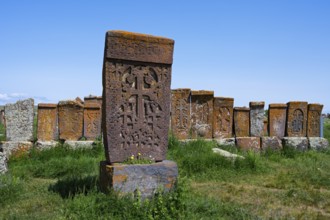 Historic Armenian crossstones stand on a green meadow under a blue sky, crossstones, khachkars,