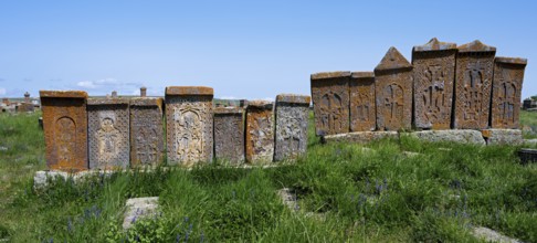 Series of engraved stone monuments on a sunny, green meadow, crossstones, khachkars, world's