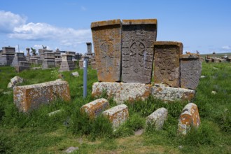 Old tombstones decorated with reliefs on a green meadow under a blue sky, crossstones, khachkars,