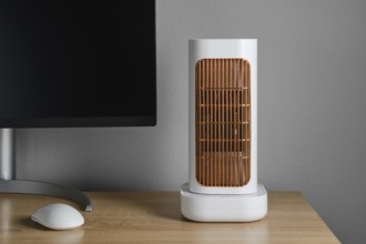 A modern electric heater is positioned on a wooden desk next to a computer monitor. The warm glow