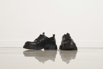 Two pairs of black loafer shoes on a shiny floor. The sleek design and minimal background create an