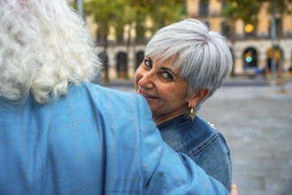 Senior woman with short gray hair smiling over her partner's shoulder as they embrace on a lively