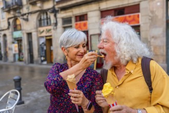 Senior couple on a charming european street sharing gelato, woman feeding man a cone as they