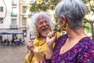 Senior couple laughing and sharing ice cream on a sunny summer date in a lively european city