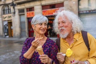 Happy senior couple eating ice cream cones while walking on a city street, sharing a sweet moment