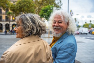 Senior couple walking in an urban environment, the man happily turning and smiling at the camera