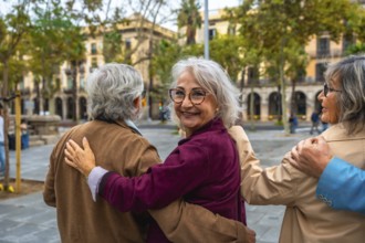 Group of three joyful senior friends walking together, hugging, and smiling at the camera in an