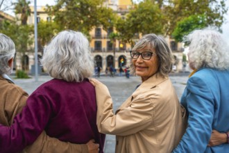 Senior friends walking together in an urban setting, the woman with glasses turning back, smiling