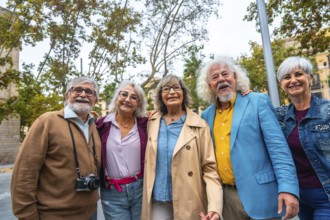 Group of five happy senior friends standing together, smiling and embracing outdoors while
