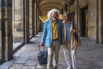 Happy senior couple smiling and holding hands while walking through a european city street, pulling