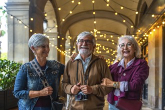 Three joyful senior friends walking arm in arm under illuminated arches, smiling and sightseeing