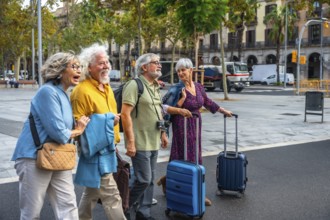 Group of happy senior friends smiling, walking along a city street and pulling luggage, enjoying