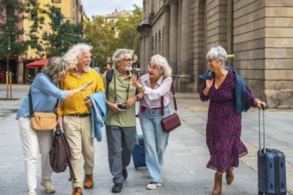 Group of happy senior friends enjoying a joyful trip, walking on a city street, carrying travel