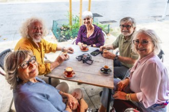 Smiling group of senior friends gathered around an outdoor cafe table, enjoying coffee,
