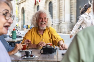 Mature man with white hair and beard laughing brightly while enjoying coffee and conversation with